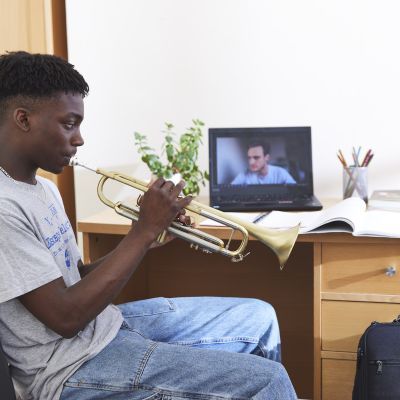 A boy sits at his desk and plays the trumpet